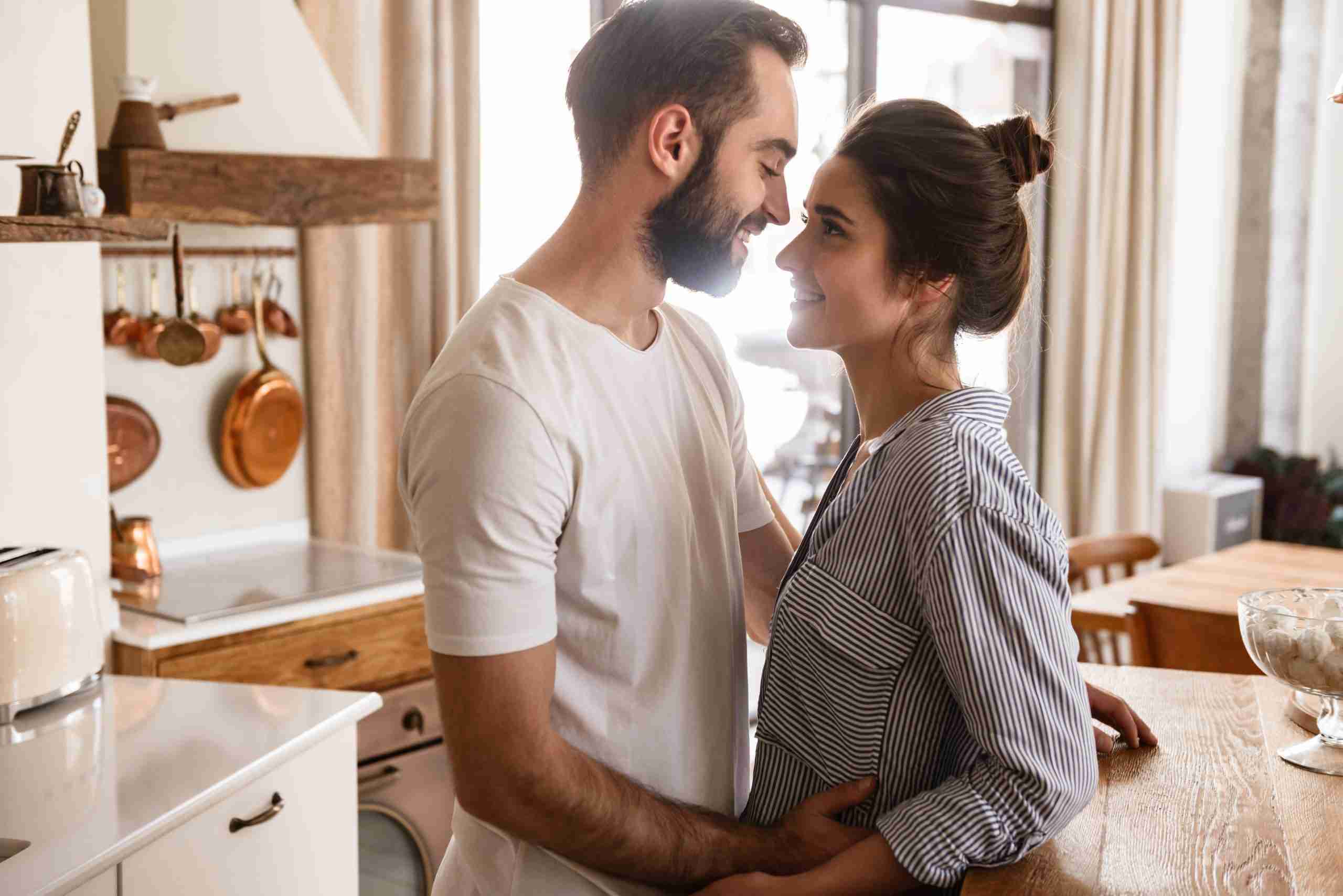 An image of a brunette man and woman looking happy and in love in their kitchen