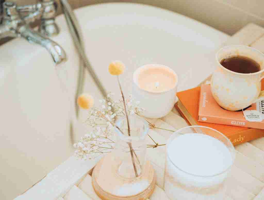 A bath board with candles, plants, books and a cup of coffee