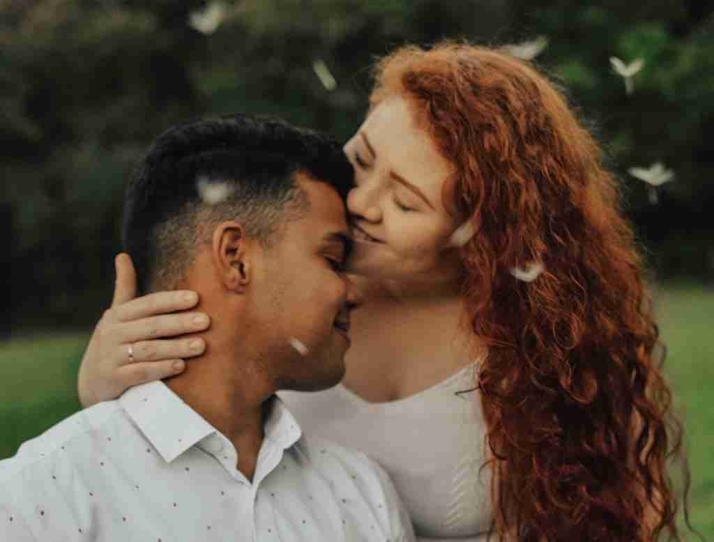 An image of a happy couple outdoors, they are smiling and the woman has her head pressed against the mans head